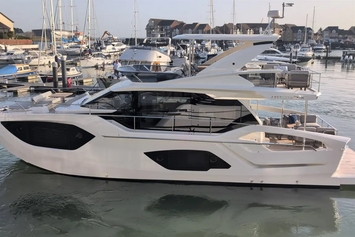 Luxurious motor yacht docked at a marina, featuring sleek design and outdoor seating, with boats and buildings in the background.
